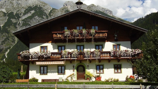 Un chalet traditionnel doté d’un balcon en bois, d’un escalier menant à l’entrée et surplombant un paysage montagneux.