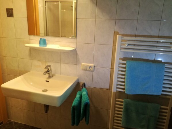 A bathroom with a sink, mirror, towel rack, and a shower area.