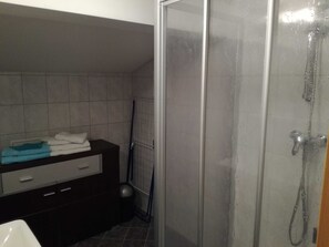 Une salle de bain avec une douche, un lavabo et un meuble-lavabo de couleur sombre, ainsi qu’une serviette.
