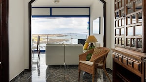 Una habitación con vista al mar, un sillón de mimbre, un sofá y un aparador de madera.