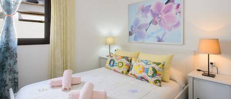 Una cama bien hecha con toallas rosas, una lámpara de noche y una obra de arte floral en la pared.