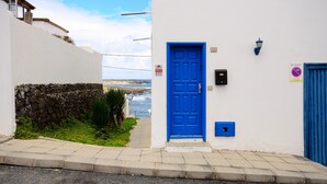 Un edificio blanco con una puerta azul, un muro de piedra y vista al mar.