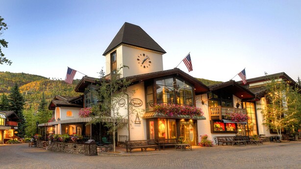 A hotel with a clock tower, outdoor seating, and American flags. - Scorpio #104 2 Bedroom Condo by RedAwning (Vail)