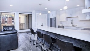 A modern kitchen with white cabinets, a stainless steel refrigerator, and a bar area with black stools. - Scorpio #104 2 Bedroom Condo by RedAwning (Vail)
