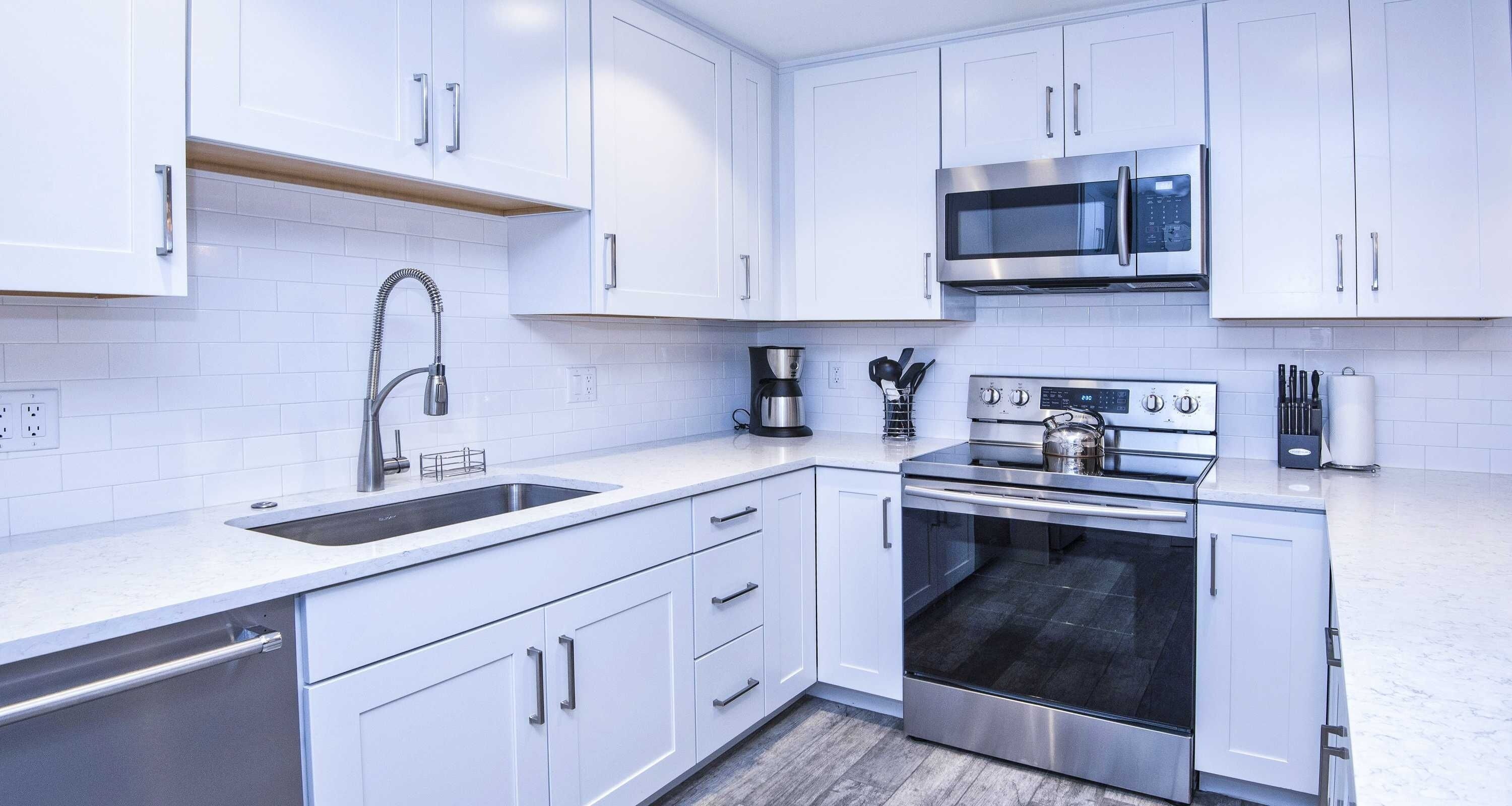 A modern kitchen with white cabinets, stainless steel appliances, a double sink, and a built-in oven.