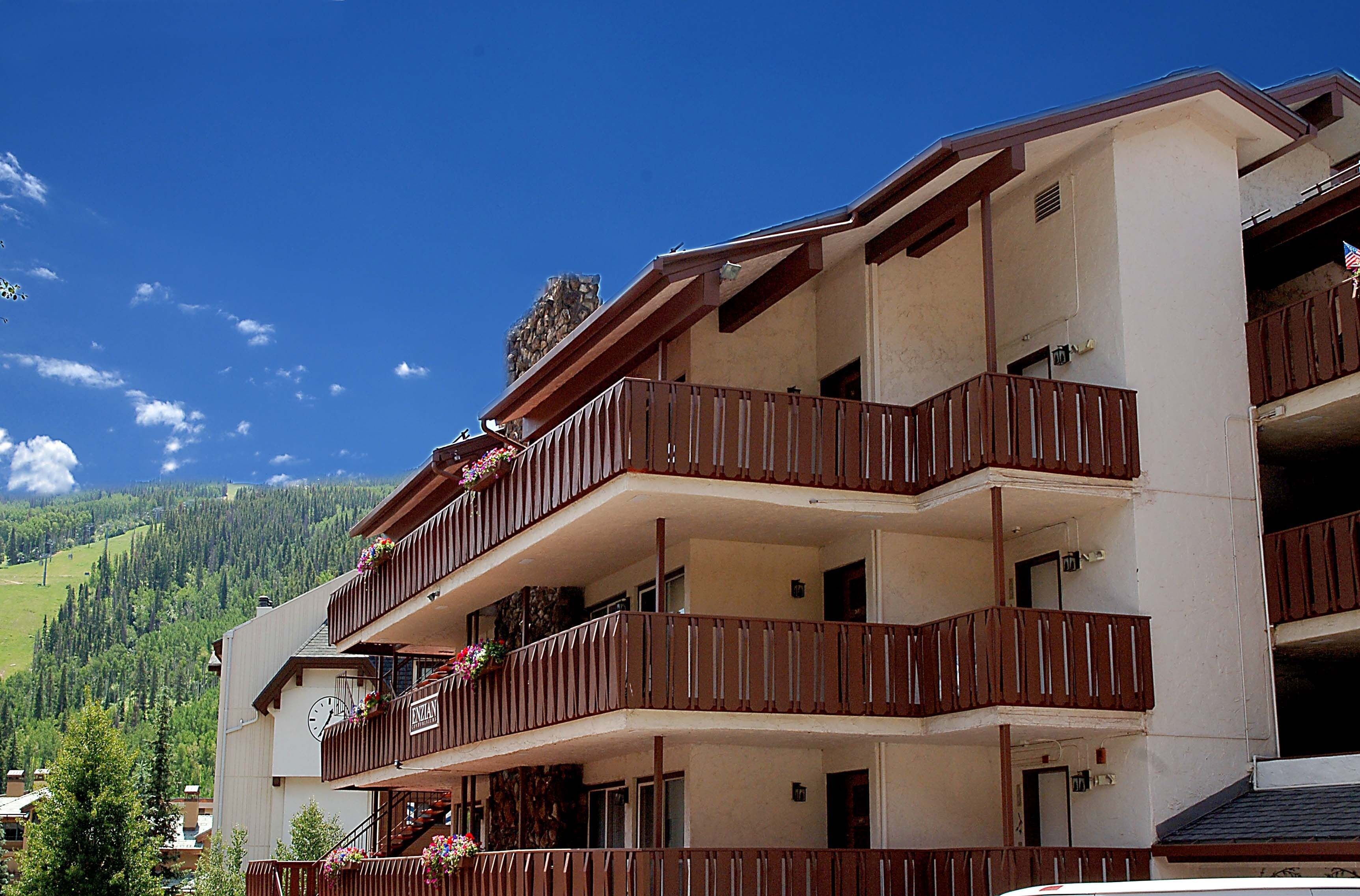 A multi-story hotel with balconies, a clock, and a view of a mountainous landscape.