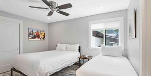 Two single beds with white linens, ceiling fan, and a window with an outside view.