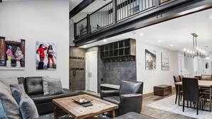 A spacious living area with a black leather sofa, a wooden coffee table, and a dining area with a wooden table and chairs.