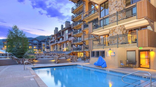 A multi-story hotel with a swimming pool, outdoor seating, and stone and wood architectural elements.
