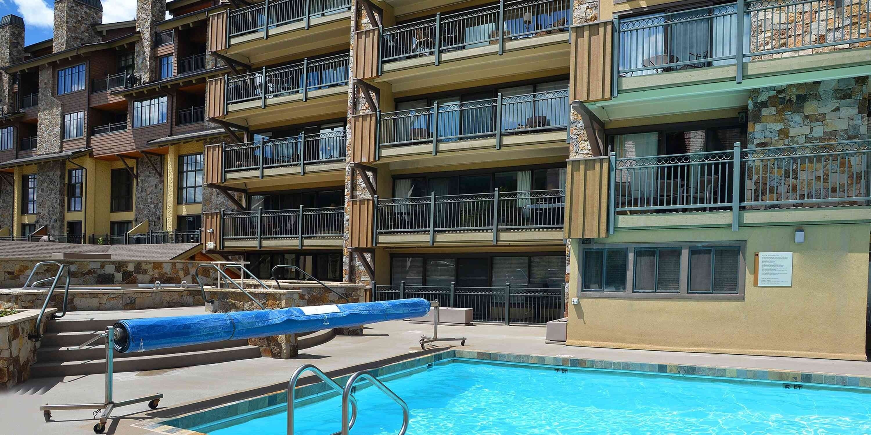 Un edificio a più piani con balconi, una piscina con copertura blu e una facciata in pietra.
