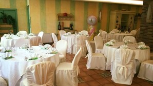 Een feestzaal met ronde tafels, witte stoelen en muren met groene strepen.
