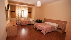 Een kamer met twee bedden, houten vloeren, een bureau, een spiegel en een raam met gordijnen met een patroon.