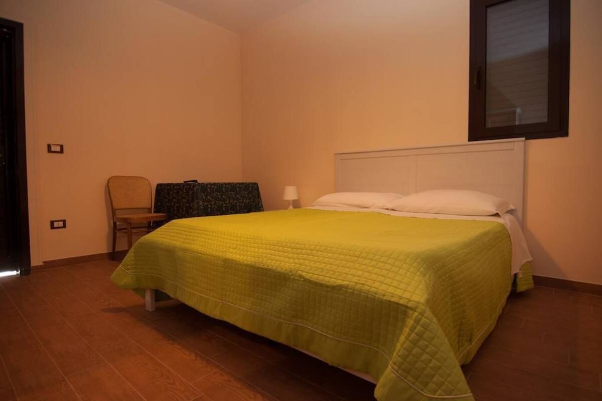 A bedroom with a bed, a chair, a nightstand, and a window.