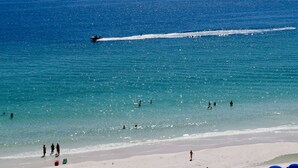 A beach scene with clear blue water, a jet ski, and people swimming and walking on the shore. - Destin Miramar Sweeping Ocean Views ~ Five Swimming Pools ~ Relaxing! End Unit.  (Destin)