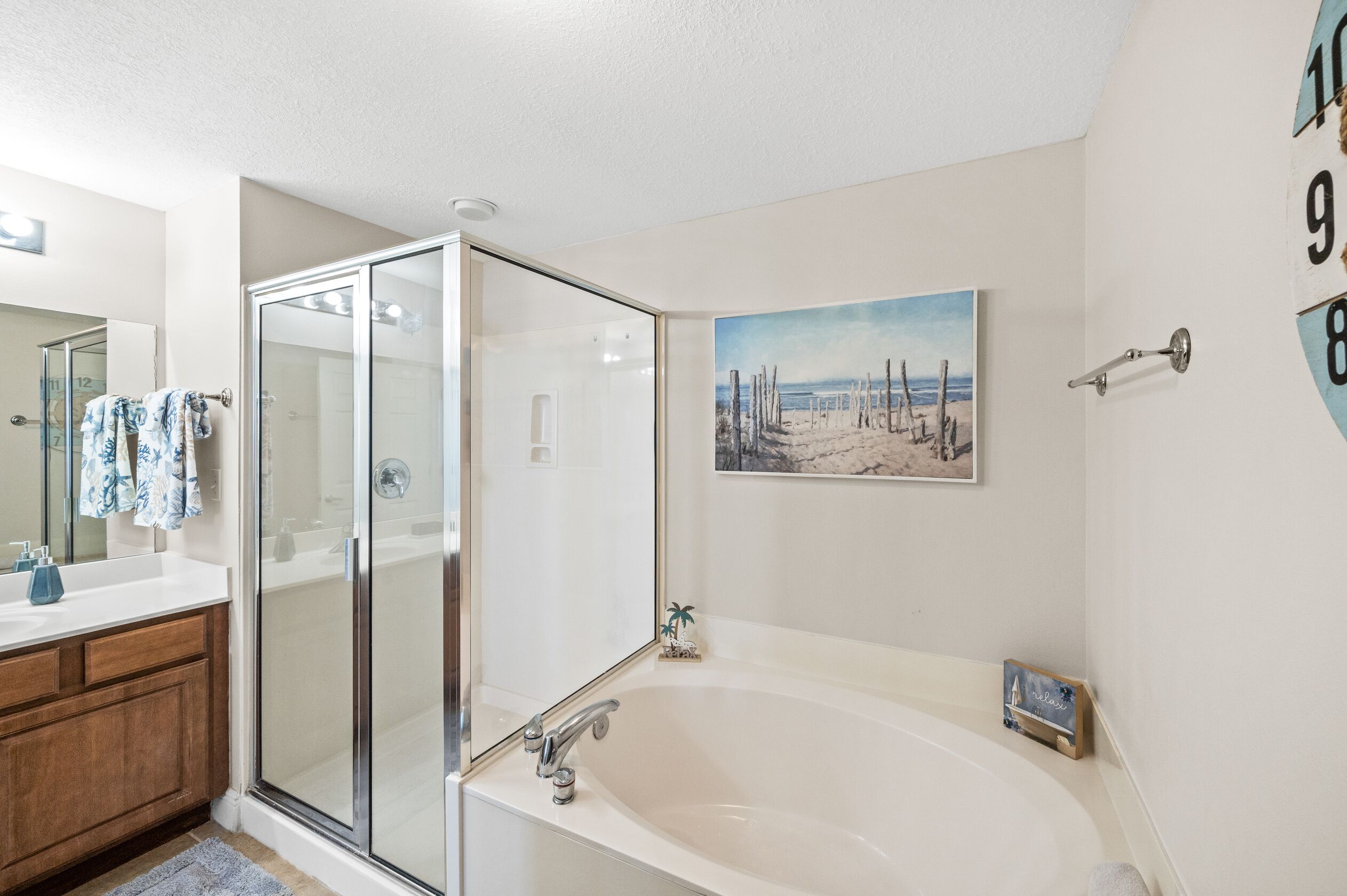 Une salle de bain moderne avec une douche à l’italienne en verre, une grande baignoire et un tableau sur le thème de la plage accroché au mur.