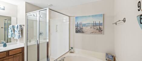Une salle de bain moderne avec une douche à l’italienne en verre, une grande baignoire et un tableau sur le thème de la plage accroché au mur.