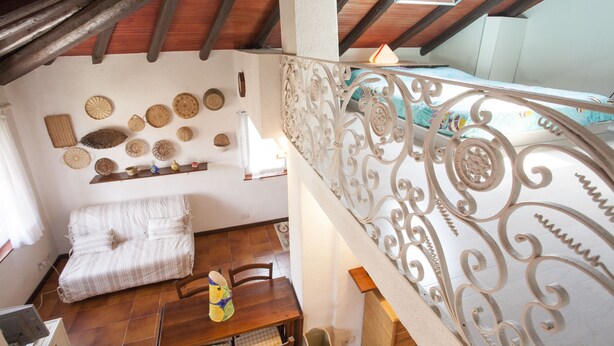 A room with a wooden ceiling, a bed, a dining table, and a decorative wall with woven baskets. - Appartamento La Perla (Marciana Marina)