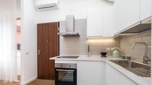 A modern kitchen with white cabinets, a built-in oven, a stainless steel sink, and a wooden door. - Accademia (Milan)