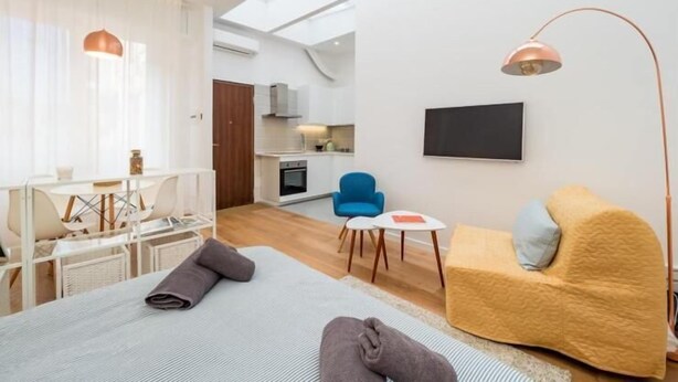A modern, open-plan living space with a dining area, a sofa, a TV, and a kitchen in the background. - Accademia (Milan)