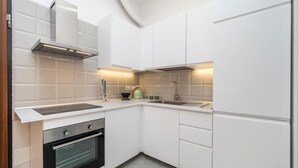 A modern kitchen with white cabinets, a stainless steel oven, and a built-in range hood. - Accademia (Milan)