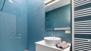 A modern bathroom with a glass shower enclosure, a white sink with a mirror above it, and a towel rack with towels. - Accademia (Milan)