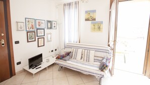 A living room with a sofa, TV, and wall art. - Appartamento Trilo Ornella (Portoferraio)