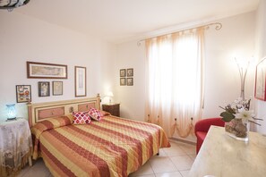 A bedroom with a bed, a nightstand, a lamp, a chair, and a table with a vase. - Appartamento Trilo Ornella (Portoferraio)