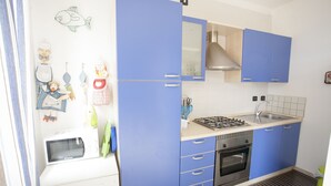 A kitchen with blue cabinets, a microwave, a stove, and a sink. - Appartamento Trilo Ornella (Portoferraio)