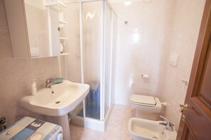 A bathroom with a sink, bidet, toilet, and a glass-enclosed shower. - Appartamento Trilo Ornella (Portoferraio)