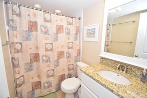 A bathroom with a shower curtain featuring sea creatures, a white toilet, a granite sink, and a mirror above the sink.