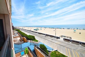 A beach view from a balcony with a wooden boardwalk, a pool, and beach umbrellas.