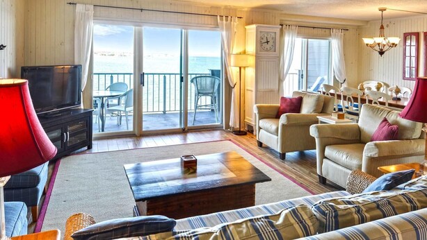 Un salon spacieux équipé d’un téléviseur, d’un canapé et de fauteuils, d’une table basse en bois et offrant une vue sur la mer grâce à de grandes portes coulissantes.