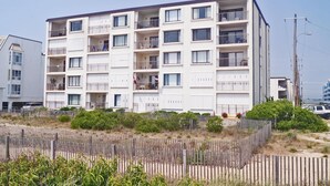 A multi-story residential building with balconies, a sandy foreground, and a clear sky. - Even Keel 404 2 Bedroom Condo by RedAwning (Ocean City)