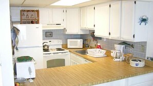 A compact kitchen with white cabinets, a microwave, a stove, and a sink. - Even Keel 404 2 Bedroom Condo by RedAwning (Ocean City)