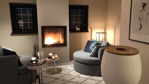 Een woonkamer met een open haard, een bank, een bijzettafeltje en een grote vaas.