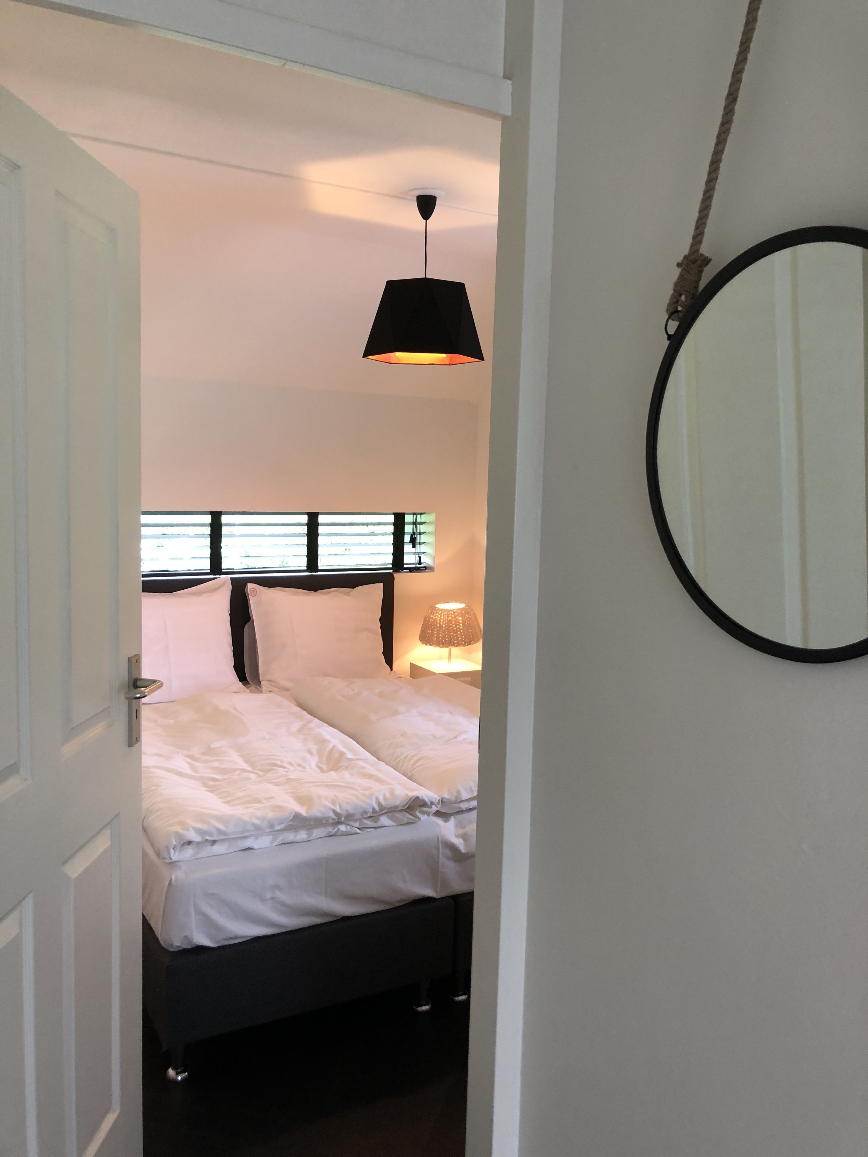Ein Schlafzimmer mit einem Bett, einer Nachttischlampe, einer Deckenleuchte und einem runden Spiegel an der Wand.