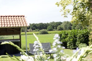 Relax in a serene outdoor setting with a hot tub, surrounded by lush greenery and a traditional tiled roof.