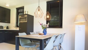 Een moderne keuken met donkere kastjes, een ingebouwde oven en een eethoek met een houten tafel en lichtblauwe stoelen.