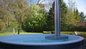 Een hottub in een tuin met bomen en een betegeld dak op de achtergrond.
