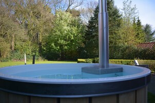 Un jacuzzi en un jardín con árboles y un techo de tejas al fondo.