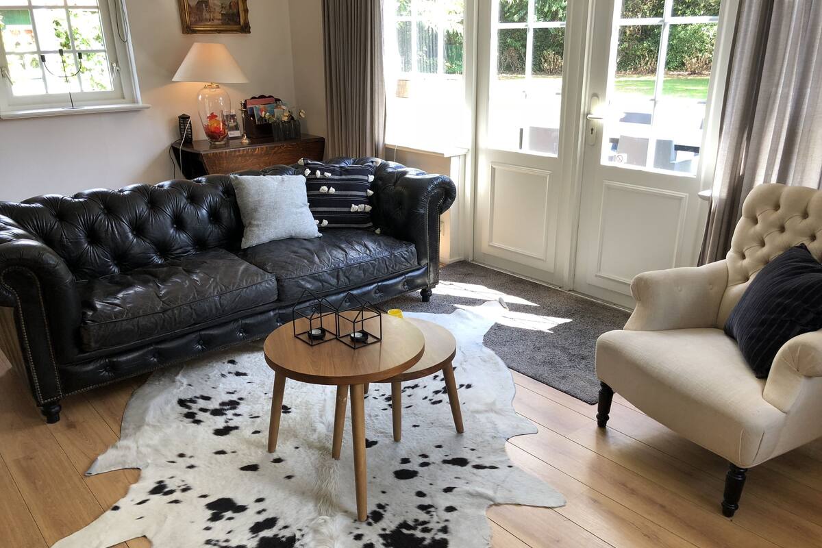 A living room with a black leather sofa, a wooden coffee table, a white armchair, and a cowhide rug.