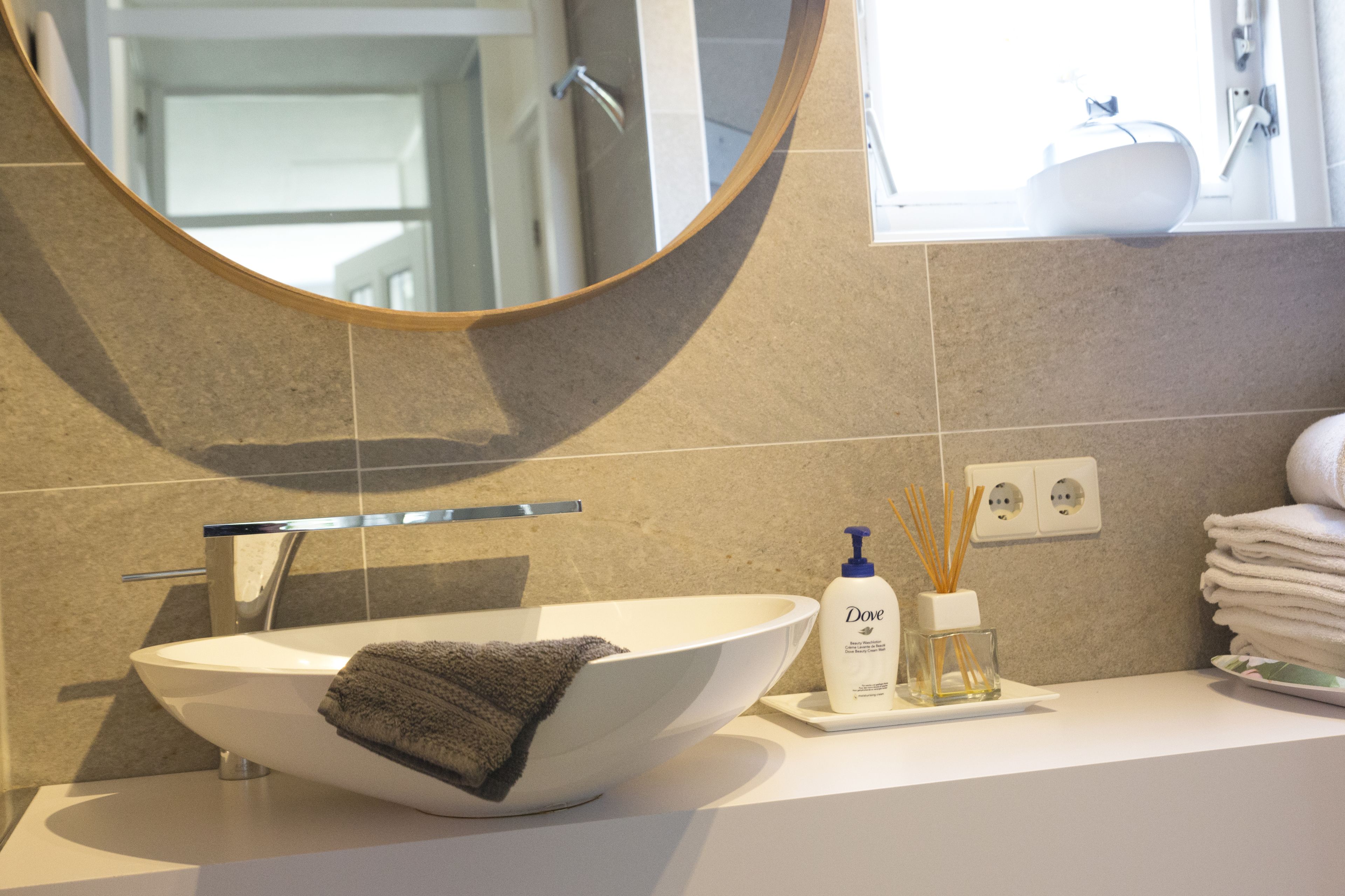A modern bathroom with a round mirror, a white sink, and a towel rack.