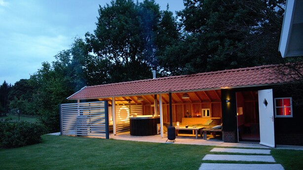 Een modern huis met een rode dakbedekking, een overdekt terras en een verzorgd gazon.
