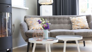 Een moderne woonkamer met een grijze bank, een witte salontafel en een decoratieve vaas met bloemen.