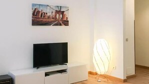 A modern living room with a flat-screen TV on a white entertainment unit, a framed cityscape picture on the wall, and a unique, illuminated chair. - Corso Sempione (Milan)