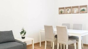 A modern living room with a grey sofa, a white dining table with four chairs, and a small white table with a plant. - Corso Sempione (Milan)