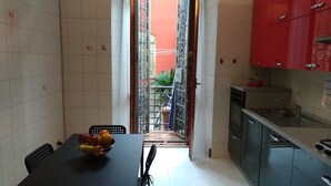 A narrow kitchen with a dining table set with fruit, a red cabinet, and a view through a metal gate to the outside. - Corso Sempione (Milan)
