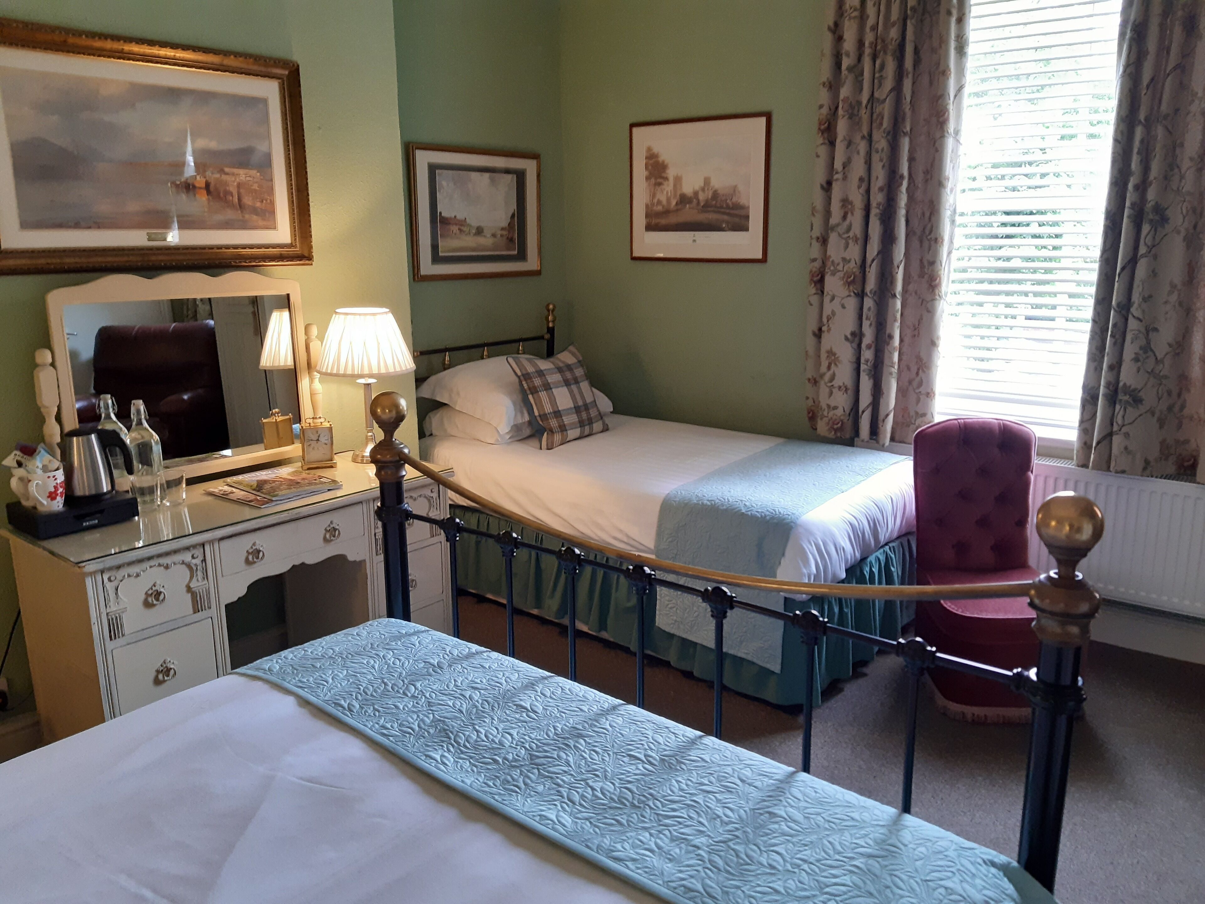 Une chambre d’hôtel avec deux lits, un bureau avec une lampe, une chaise et des tableaux encadrés aux murs.