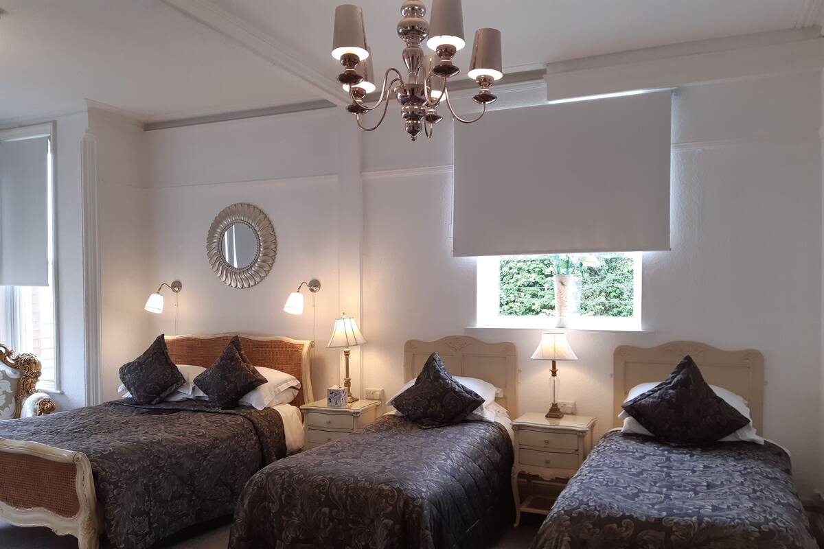 A hotel room with two beds, a chandelier, a mirror, and a window with a view of greenery.