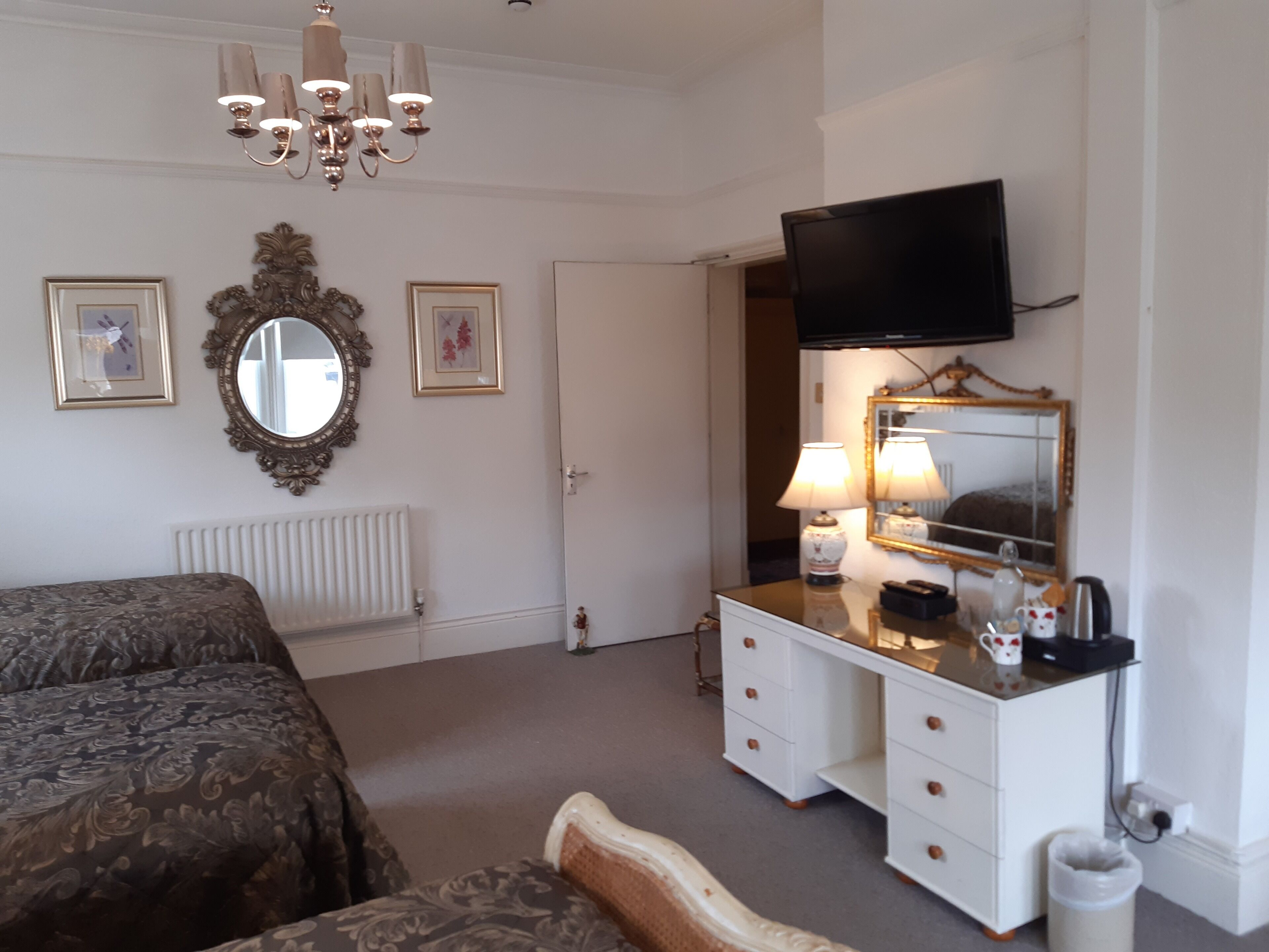 A bedroom with a bed, a dresser, a television, a mirror, and a chandelier.